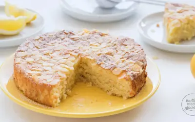 Saftiger mandelkuchen rezept, bestäubt mit Puderzucker und Mandelsplittern, daneben Zitronenspalten und eine ganze Zitrone.