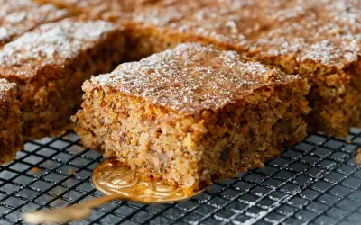 Ein saftiger karottenkuchen glutenfrei, bestäubt mit Puderzucker, wird auf einem Gitter präsentiert.