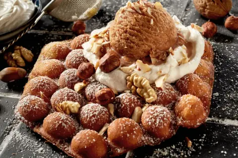 Bubble Eis auf einem Waffel-Snack, bestreut mit Puderzucker und garniert mit Nüssen und einer Kugel Eis.
