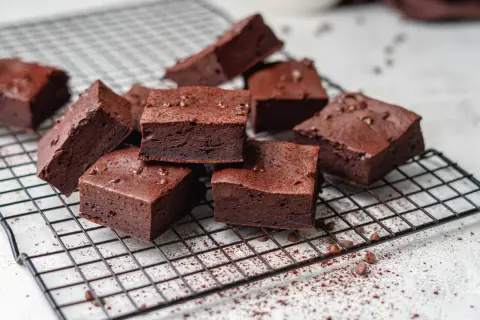 Saftige low carb brownies, bestreut mit Kakaopulver und Schokostückchen, auf einem Kuchengitter.