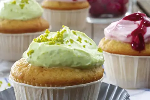 Zwei Cupcakes mit cremiger, grüner Pistazien-Frosting und ein weiterer mit rosa Beeren-Frosting.