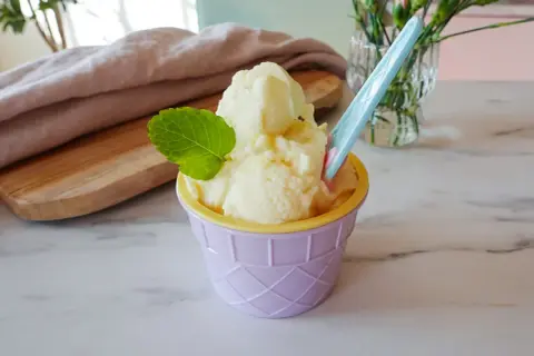 Ein cremiges Ananas Eis in einem lila Becher, garniert mit Minze. Perfekt für heiße Tage!