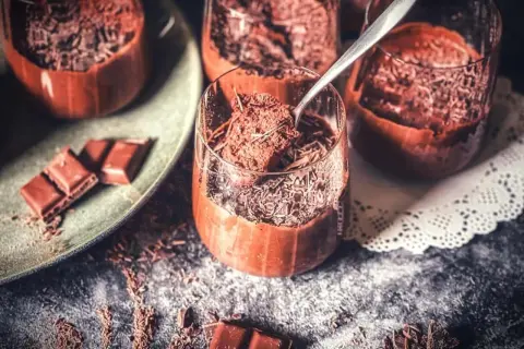 Schokoladenmousse ohne Ei, garniert mit Schokostreuseln. Ein Löffel hebt eine Portion aus dem Glas.