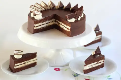 Schokoladentorte mit cremiger Füllung und Schokostückchen, inspiriert von der Kinder Pingui Torte. Serviert auf einem Tortenständer mit einzelnen Tortenstücken.