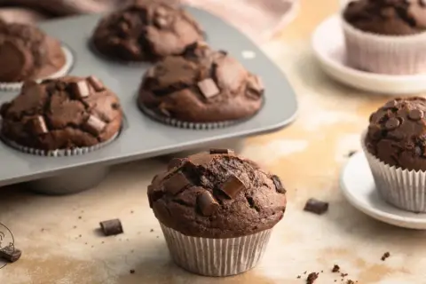 Schokomuffins mit Schokostückchen, perfekt für Kinder. Ein Muffin liegt vorne, weitere im Blech und auf Tellern.