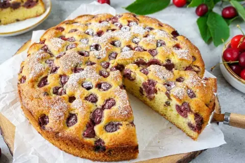 Saftiger Kuchen mit Kirschen, bestäubt mit Puderzucker. Ein Stück wurde bereits herausgeschnitten.