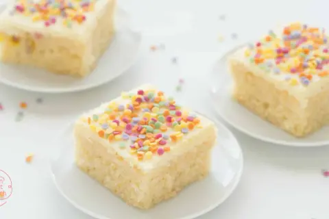 Drei Stücke saftiger konfetti kuchen mit weißer Glasur und bunten Streuseln auf weißen Tellern.