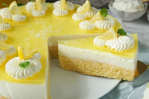 Eine köstliche zitronen torte mit Biskuitboden, cremiger Füllung und gelber Zitronenglasur, verziert mit Sahnetuffs und Zitronenspalten.