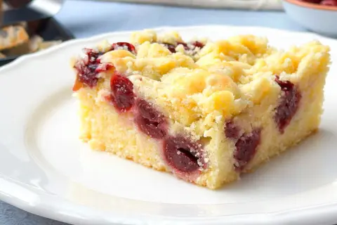 Ein saftiges Stück Kirsch-Streuselkuchen vom Blech, mit vielen Kirschen und knusprigen Streuseln, auf einem weißen Teller.