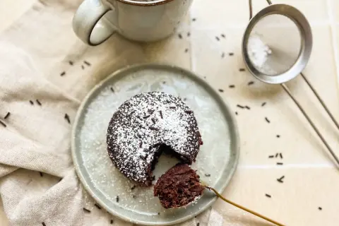 Ein saftiger Schoko-Tassenkuchen ohne Ei, bestäubt mit Puderzucker und Schokostreuseln, bereit zum Genießen.