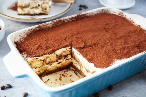 Ein cremiges Tiramisu, perfekt für ein tiramisu rezept ohne alkohol. Mit Kakaopulver bestäubt und in einer blauen Auflaufform serviert.