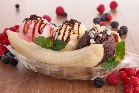 Ein köstlicher Bananensplit Eis mit drei Kugeln Eis, garniert mit Beeren und Minze.