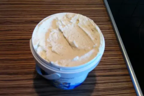 Ein Behälter mit cremigem, selbstgemachtem laktosefreiem Eis steht auf einer Holzoberfläche.