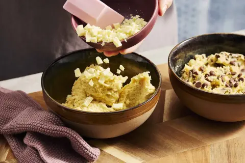 Zutaten für ein Crumble Cookie Rezept werden in Schüsseln gegeben: Teig mit Schokostückchen und weißer Schokolade.