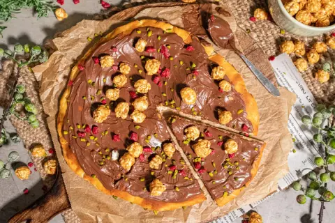 Eine köstliche Nutella Pizza, belegt mit karamellisiertem Popcorn und gehackten Pistazien, bereit zum Genießen.