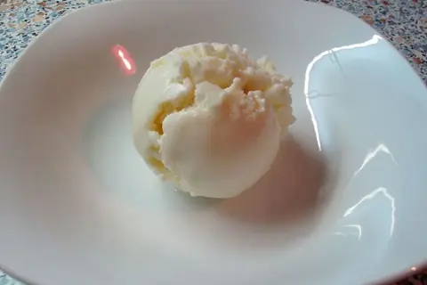 Ein Löffel cremiges Eis aus Quark in einer weißen Schale.