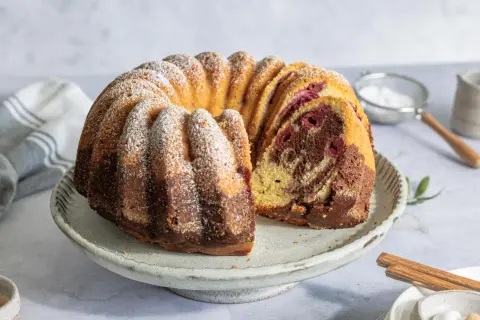 Ein saftiger Marmorkuchen mit Kirschen, bestäubt mit Puderzucker, auf einem rustikalen Kuchenständer.