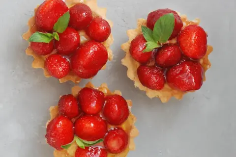 Drei köstliche Erdbeer Tartelettes, garniert mit frischer Minze, auf grauem Untergrund.