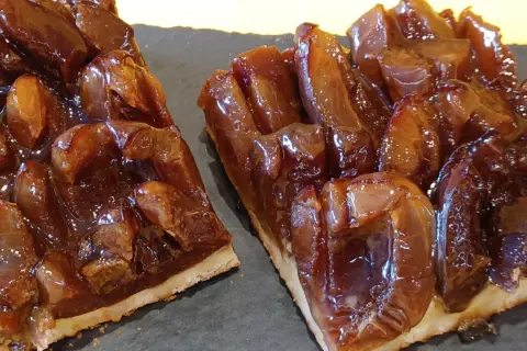 Zwei Stücke saftiger Zwetschgenkuchen vom Blech, glänzend und karamellisiert, auf dunkler Platte angerichtet.