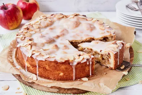 Ein köstlicher gedeckter Apfelkuchen mit zarter Glasur und Mandelblättchen, daneben ein Stück Apfelmus.