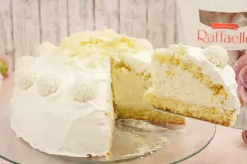 Eine köstliche Raffaello Torte, verziert mit Kokosraspeln und weißer Schokolade. Ein Stück wird gerade serviert.