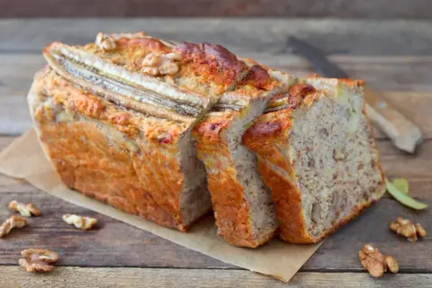 Saftiger bananenkuchen vegan, mit Nüssen und Bananenstücken, auf einem Holztisch.