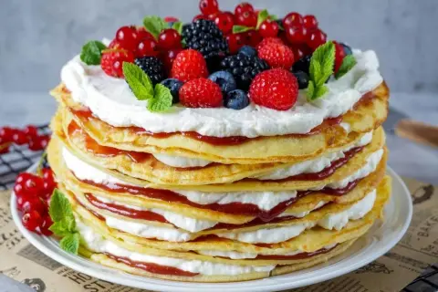 Eine hohe Pfannkuchen Torte mit Sahne und roter Marmelade, gekrönt mit frischen Beeren und Minze.