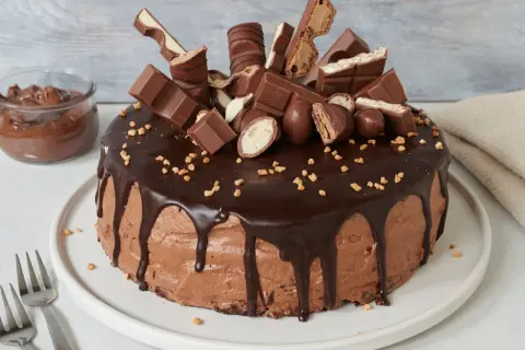 Eine üppige Nutella Torte, dekoriert mit Schokoriegeln und Nüssen. Daneben ein Glas Nutella.