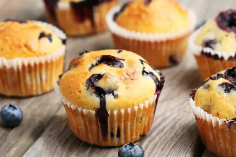 Saftige Blaubeermuffins, perfekt für ein Blaubeermuffins Rezept. Frisch gebacken und auf rustikalem Holz angerichtet.