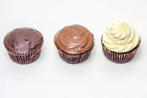 Drei Cupcakes: einer mit dunkler Ganache, einer mit Milchschokoladen-Ganache und einer mit weißer Creme. Perfekt für ein schnelles Ganache Rezept.