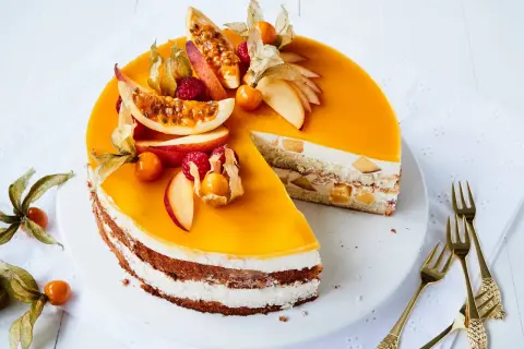 Eine köstliche Pfirsich Maracuja Torte, dekoriert mit frischen Früchten und Physalis. Ein Stück ist bereits angeschnitten.