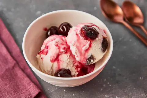 Zwei Kugeln cremiges Eis mit einem Hauch von Amarena Kirschen und ganzen Kirschen garniert.