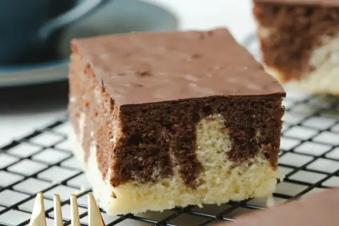 Ein Stück saftiger Marmorkuchen vom Blech mit Schokoladenglasur auf einem Kuchengitter.