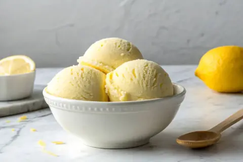 Erfrischendes Limoncello Eis in einer Schale, daneben eine Zitrone und ein Löffel.