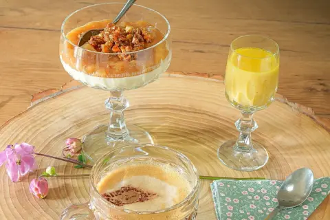 Ein Dessert im Glas mit Rhabarberkompott und Streuseln, daneben ein gelbes Getränk und ein Kaffee.