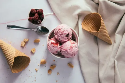 Schüssel mit rosa Eiskugeln, Kirschen und Waffelhörnchen. Ein süßer Genuss, der trotz der Kalorien verlockt.