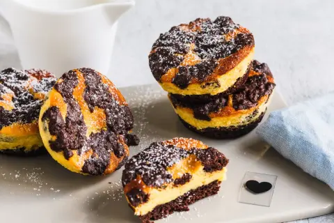 Leckere zupfkuchen muffins mit Puderzucker bestäubt, daneben ein Milchkännchen und ein blaues Tuch.