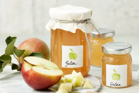 Zwei Gläser mit selbstgemachtem Apfelgelee, daneben frische Äpfel und Apfelstücke. Ein leckeres Apfelgelee Rezept zum Nachmachen.