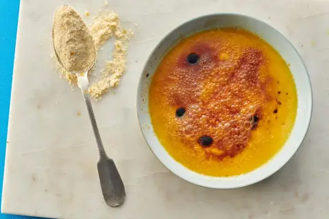 Creme brulee mit karamellisierter Zuckerkruste und Bläschen, daneben ein Löffel mit feinem Zucker.