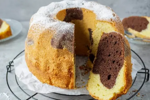 Ein saftiger Marmorkuchen, der zeigt, wie einfach backen sein kann. Mit Puderzucker bestäubt und einem Stück herausgeschnitten.