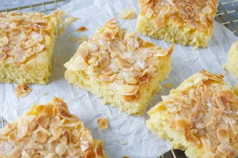 Saftiger Buttermilch Kuchen mit knusprigen Mandelblättchen und Zucker bestreut, auf Backpapier und einem Gitterrost.