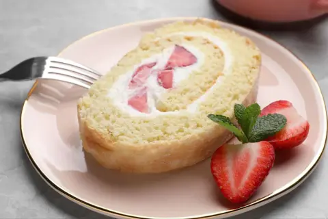 Ein Stück Biskuitrolle mit Erdbeeren und Sahne, perfekt für ein leichtes Dessert. Dieses Biskuitrolle Rezept ist ein Genuss!