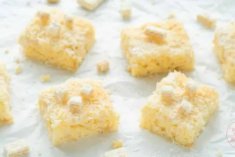 Saftige Stücke Buttermilch Kokos Kuchen, bestreut mit Kokosraspeln und kleinen weißen Würfeln, verlocken zum Genuss.