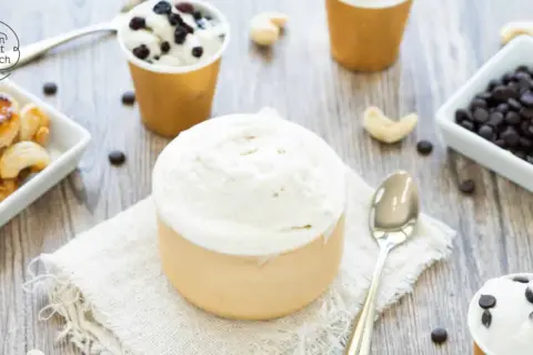 Cremiges Vanilleeis ohne Ei, serviert in Bechern, mit Cashews und Schokodrops daneben.