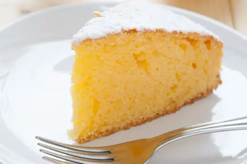 Ein saftiges Stück Vanille Kuchen, bestäubt mit Puderzucker, wartet auf dem Teller neben einer Gabel.