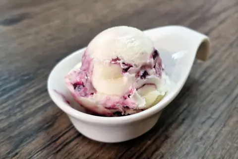Cremiges Cheesecake Eis mit fruchtigen Beerenwirbeln in einer weißen Schale auf Holztisch.