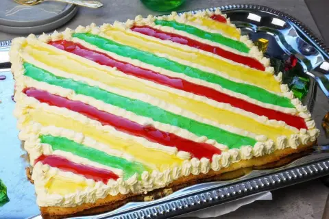 Bunte Philadelphia Torte mit Waldmeister-Aroma, dekoriert mit Sahnetuffs und roten Fruchtstreifen.