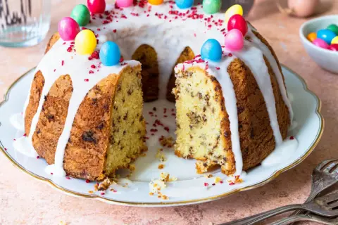Ein Gugelhupf mit Schokoladenstückchen, Zuckerguss und bunten Ostereiern. Dieses Gugelhupf Rezept ist perfekt für Ostern.