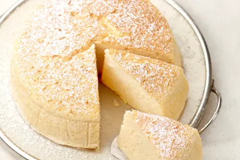 Ein luftiger, fluffiger japanischer Cheesecake, bestäubt mit Puderzucker, auf einer Servierplatte.