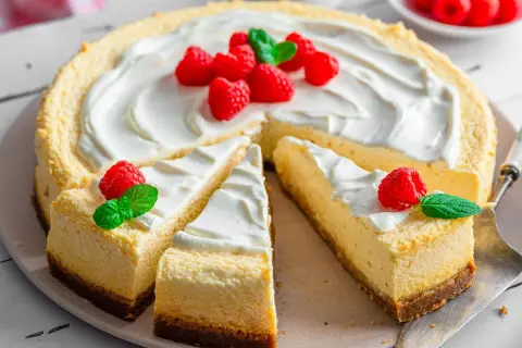Ein New York Cheesecake, dekoriert mit frischen Himbeeren und Minze, wartet darauf, genossen zu werden.